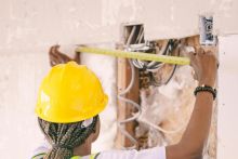 Back view of a construction worker measuring wall space wearing safety gear.